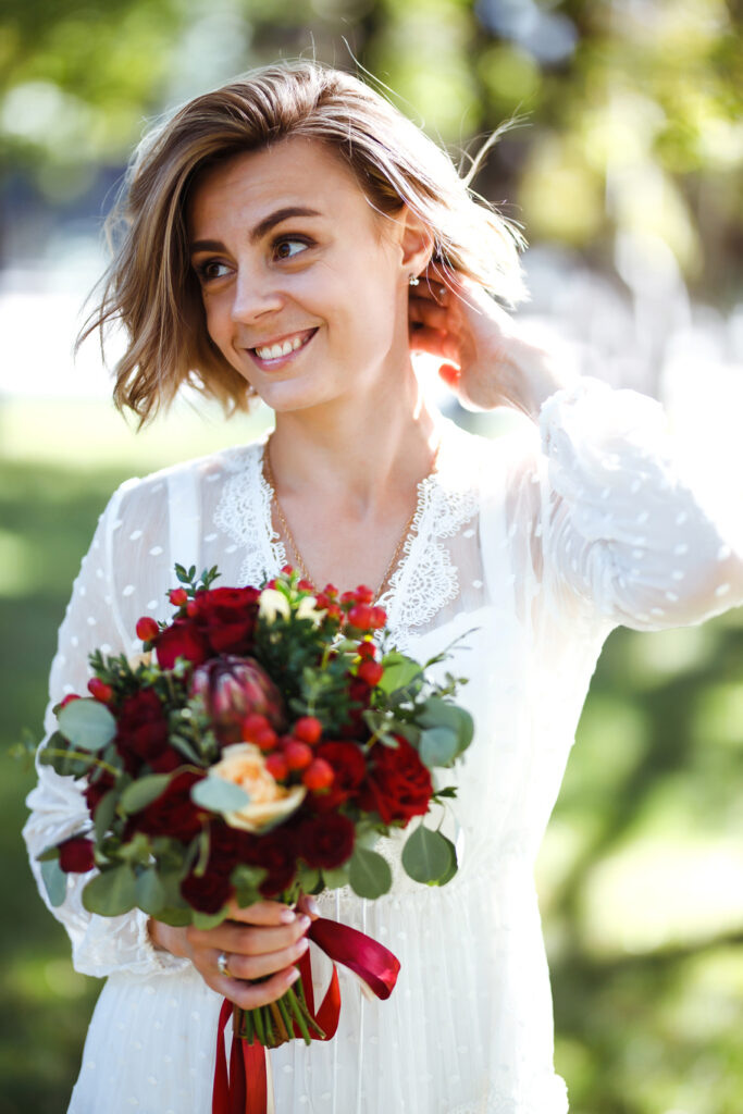 Όμορφη νύφη με γαμήλια ανθοδέσμη στο πάρκο. Κομψή γυναίκα με επαγγελματικό μακιγιάζ και στυλ μαλλιών