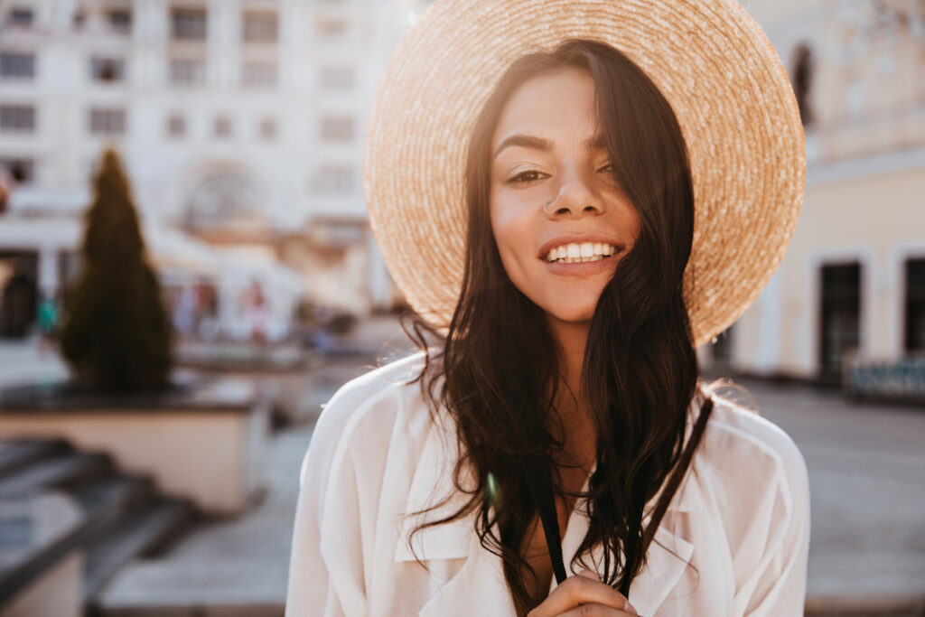 Εξωτερική φωτογραφία γυναίκας με κομψό καπέλο που χαλαρώνει σε ηλιόλουστη μέρα στην πόλη