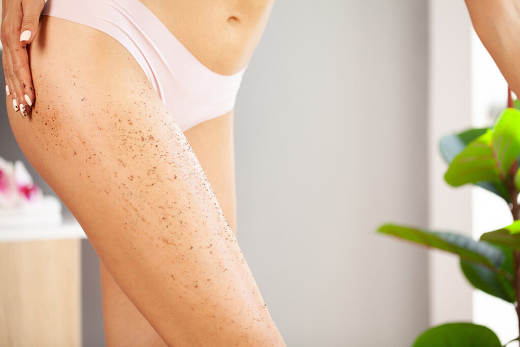 Όμορφη νεαρή γυναίκα που εφαρμόζει scrub σώματος στο πόδι στο σπίτι.