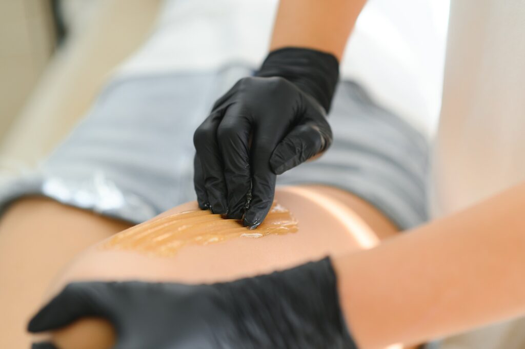 χέρι με γάντι που απλώνει προϊόν μαυρίσματος σε σώμα γυναικείο