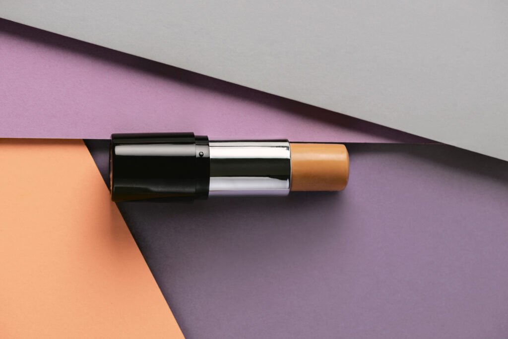 Στικ foundation σε μοντέρνο φόντο με γεωμετρικά σχήματα.