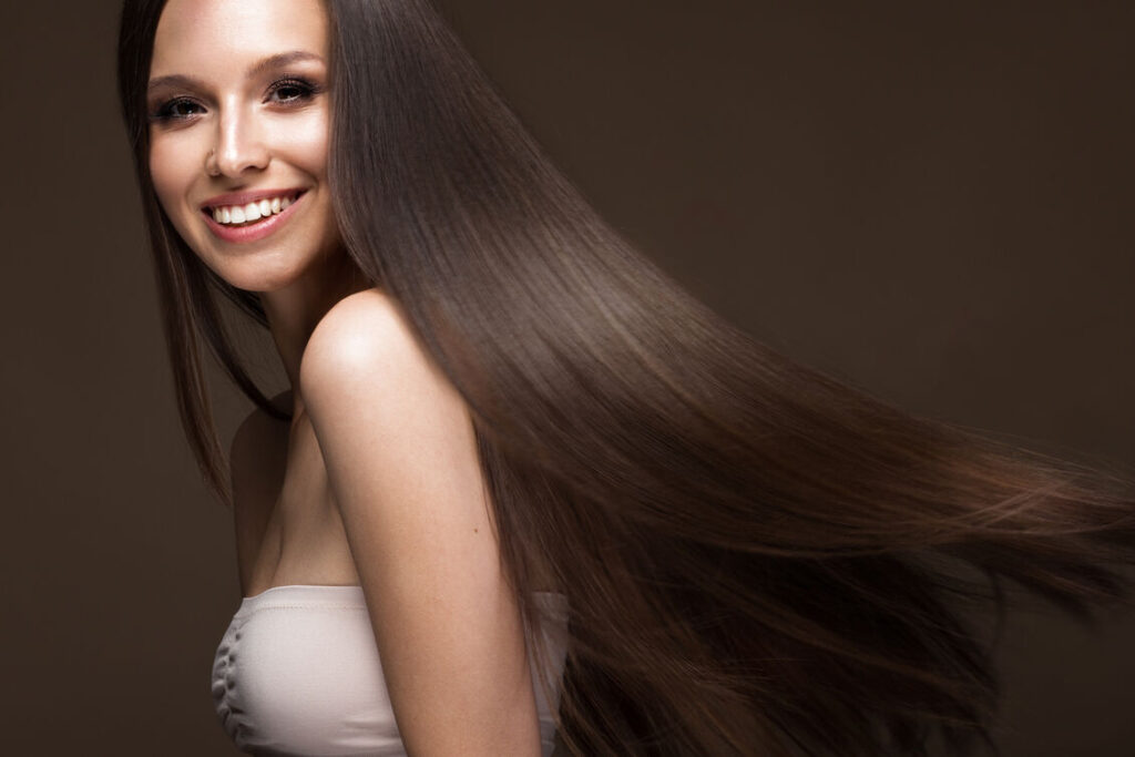 Όμορφη γυναίκα που χαμογελάει με καστανά μακριά υγιή μαλλιά σε κίνηση