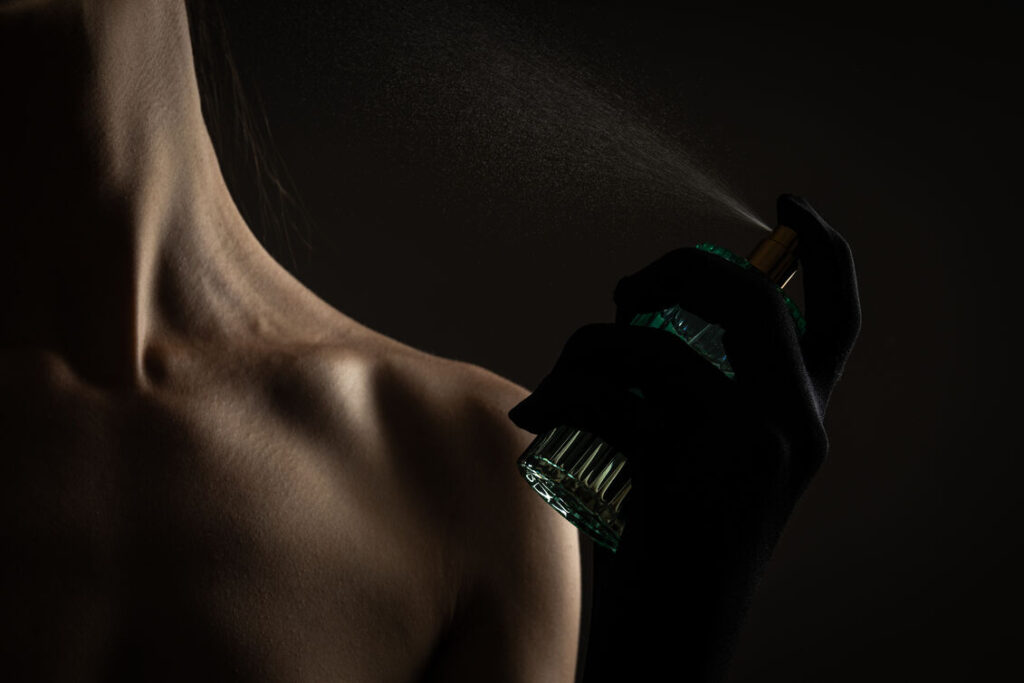 νεαρή γυναίκα που εφαρμόζει άρωμα σε μαύρο φόντο